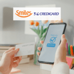 mão efetuando segurando cartão de crédito e celular efetuando pagamento com logo Smiles e Credicard