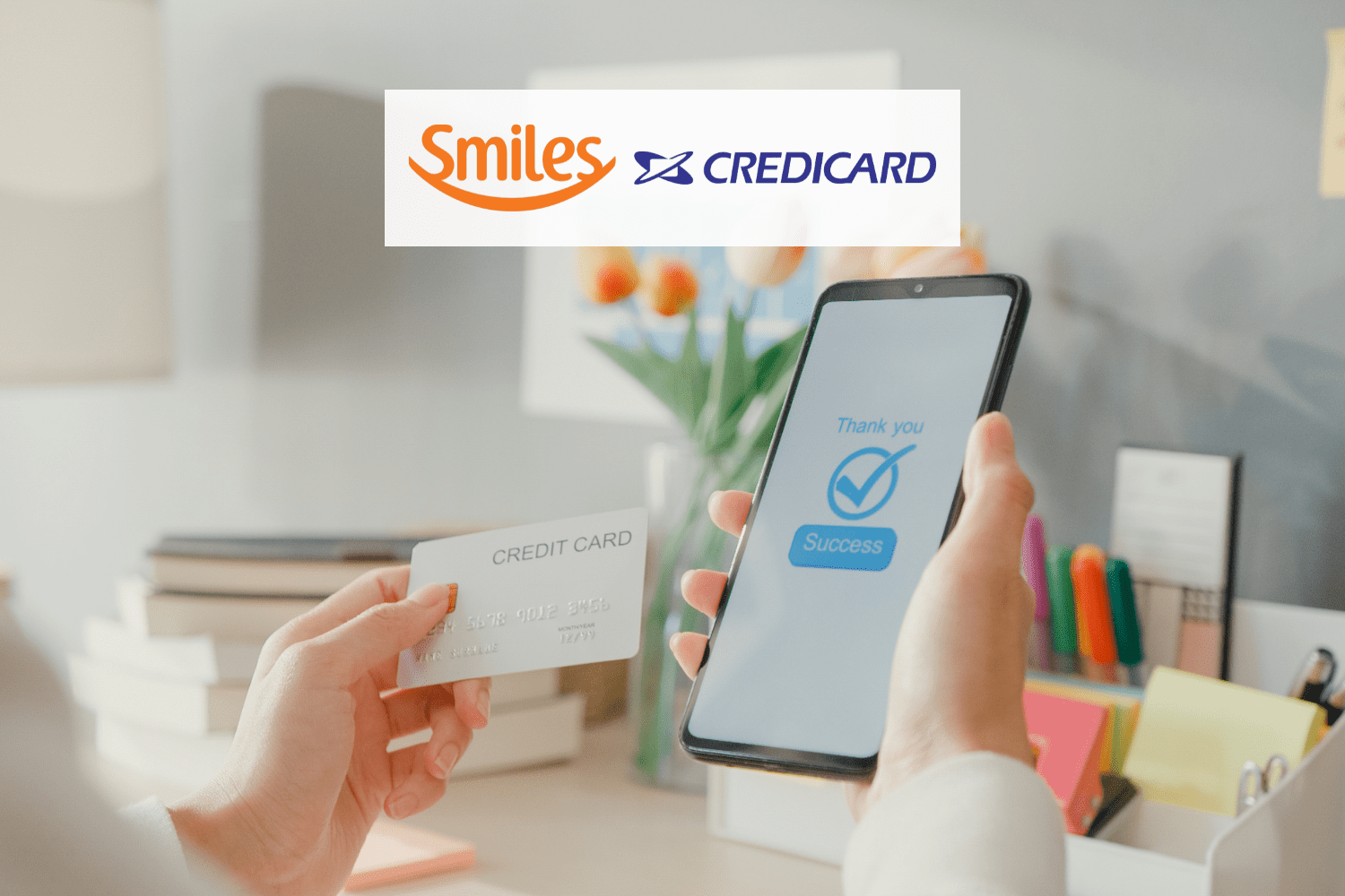 mão efetuando segurando cartão de crédito e celular efetuando pagamento com logo Smiles e Credicard