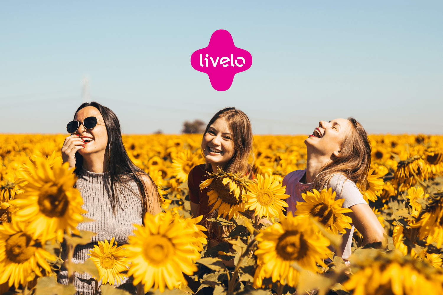 grupo de amigas sorrindo em um jardim de girassol com logo Livelo