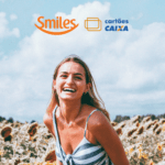 mulher branca loira sorrindo em um jardim com logo Smiles e Caixa