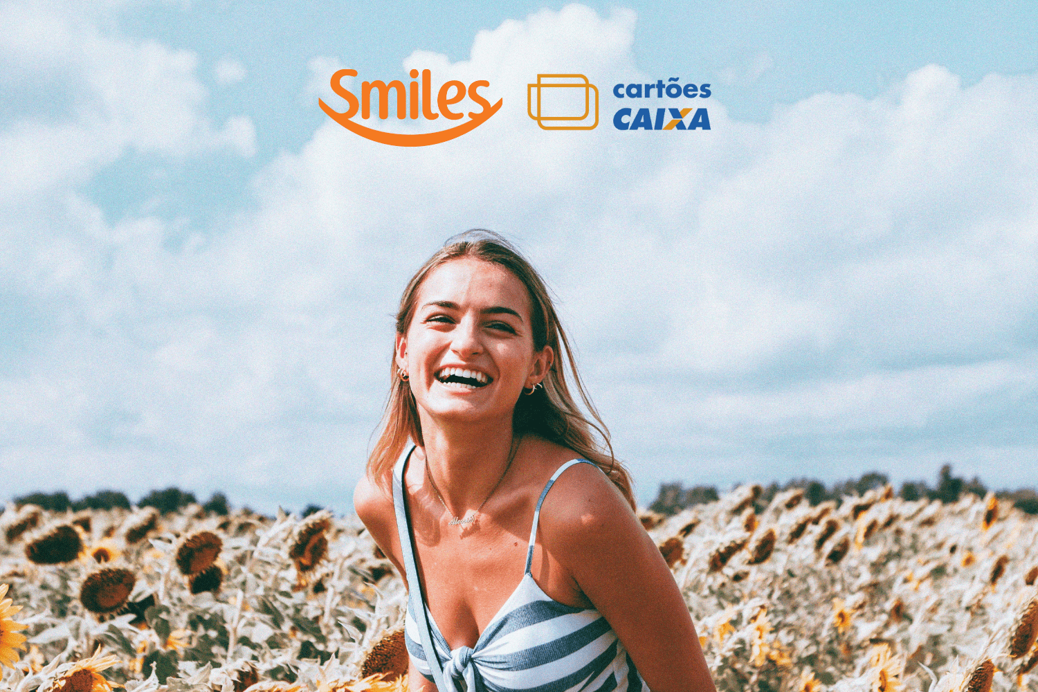 mulher branca loira sorrindo em um jardim com logo Smiles e Caixa