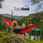 mulher loira deitada em uma rede olhando o horizonte com logo TudoAzul