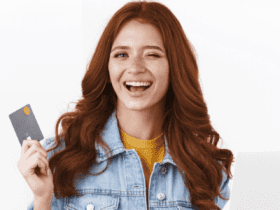 Mulher branca ruiva segudando um cartão e notebook piscando para a câmera com logo Esfera