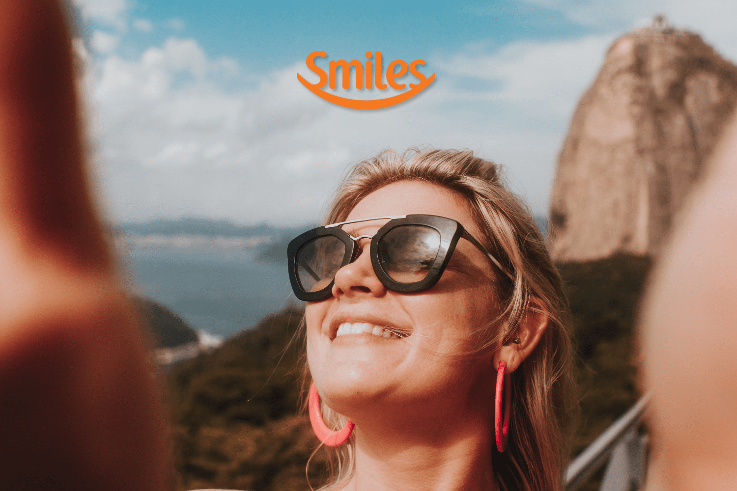 mulher loira com óculos de sol e sorridente com logo Smiles Clube Smiles