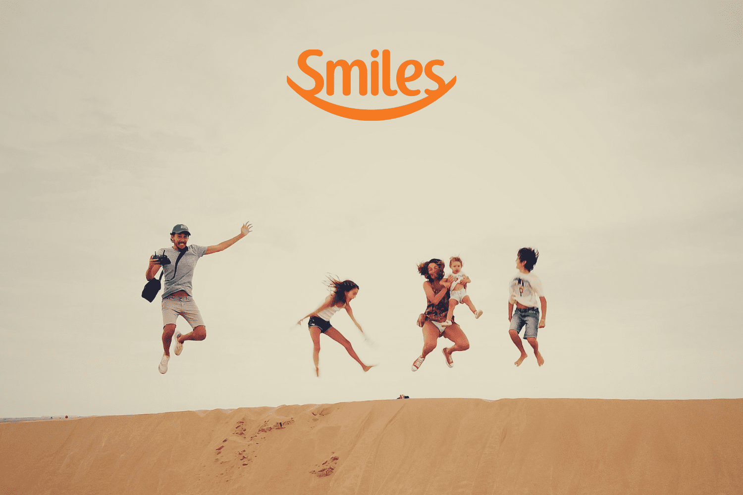 família pulando alegre sobre a areia com logo Clube Smiles