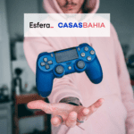 Pessoa jogando um controle de vídeo game com logo Esfera e Casas Bahia 10 pontos Esfera