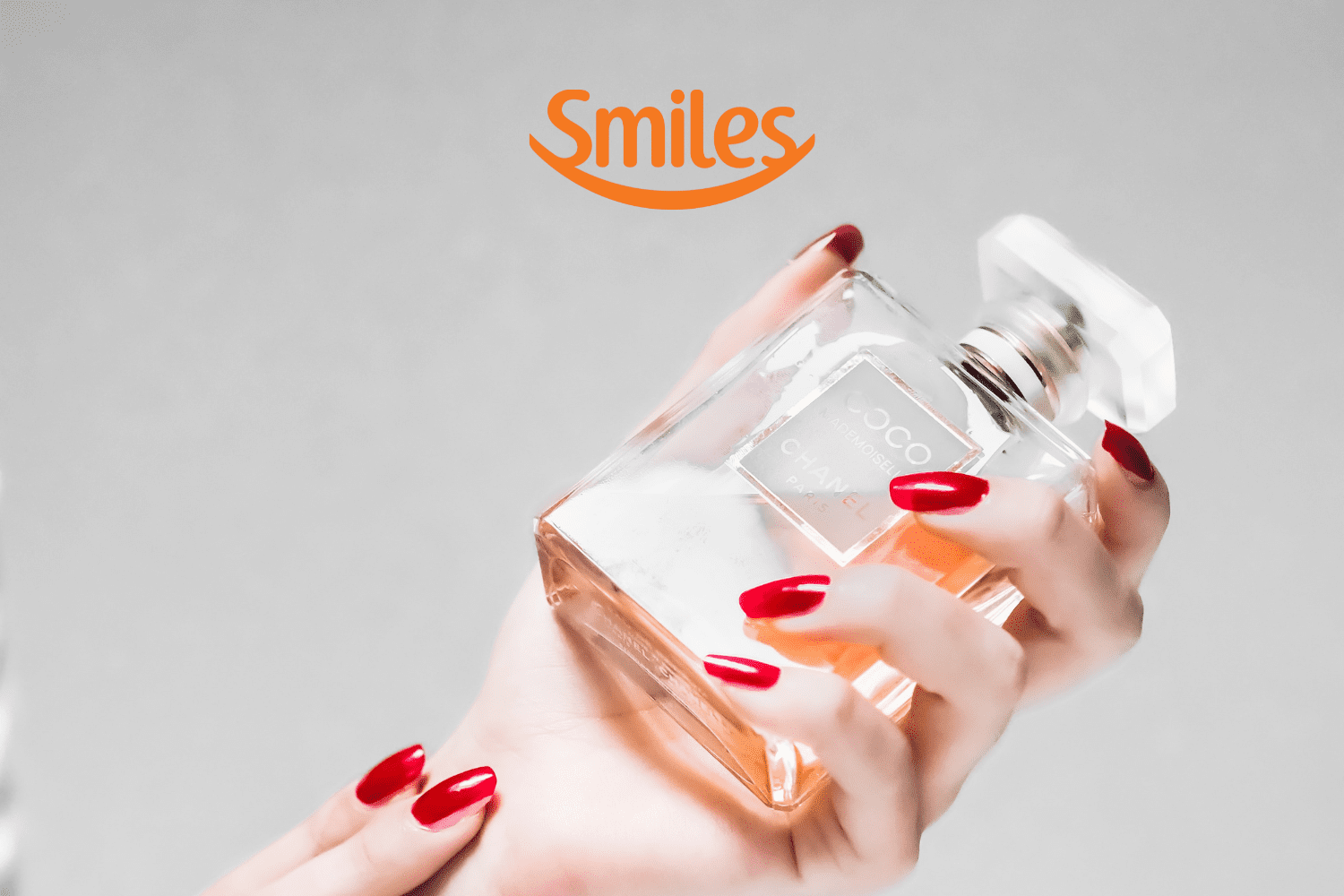 uma mão segurando um frasco de perfume com logo Smiles Pontos Smiles