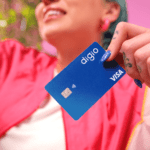 mulher branca com cabelo azul sorrindo e segurando um cartão de crédito Digio