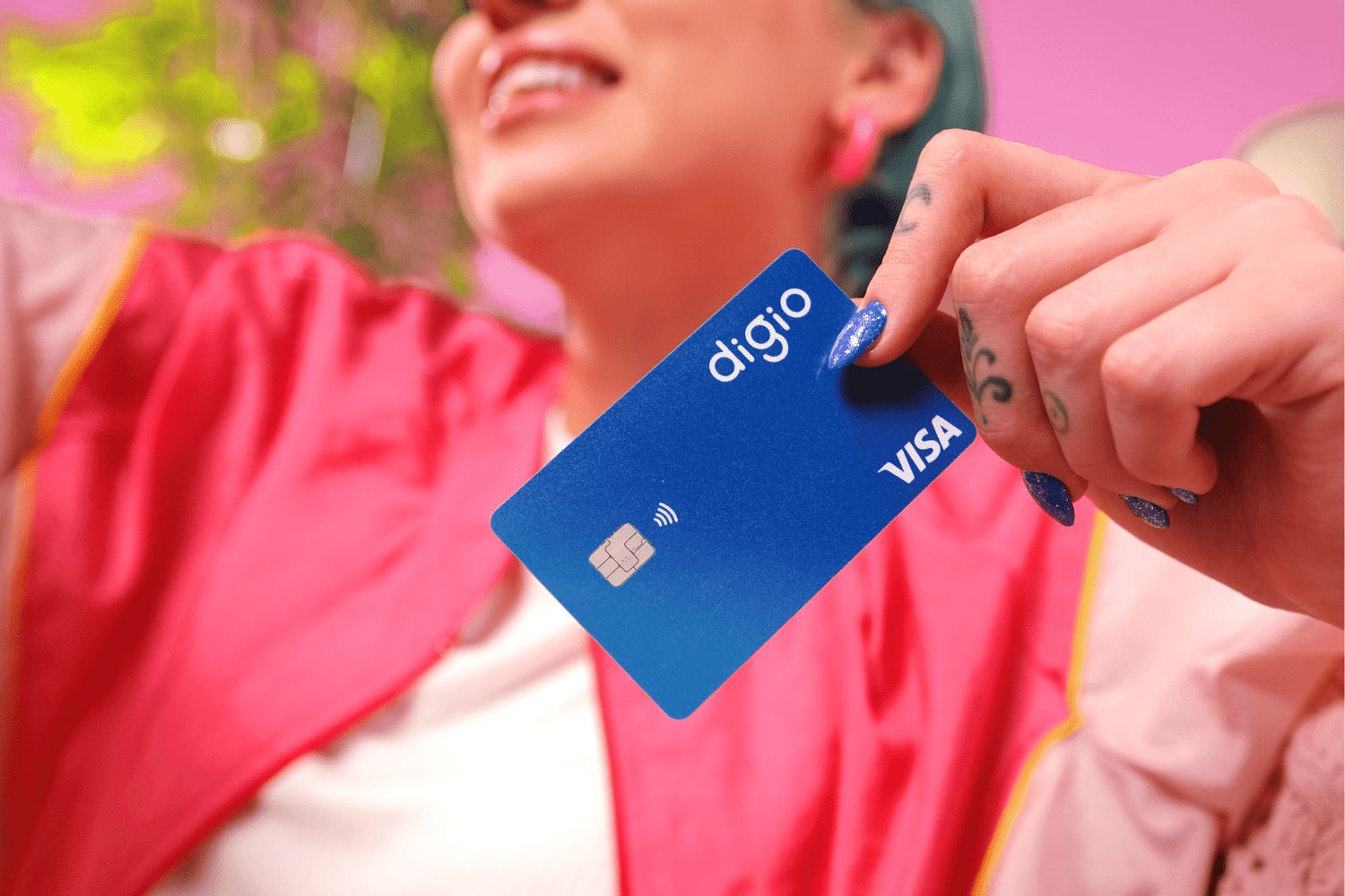 mulher branca com cabelo azul sorrindo e segurando um cartão de crédito Digio