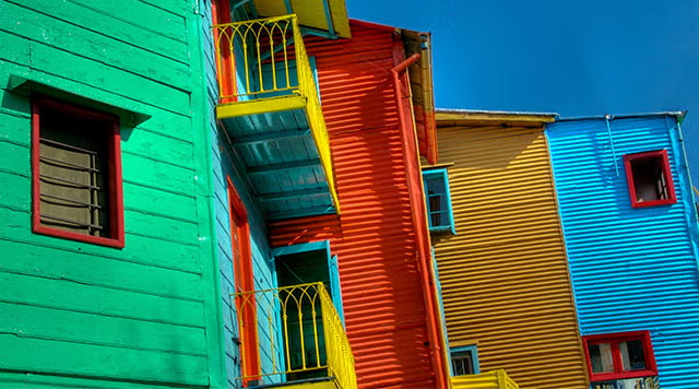 Casas coloridas, a da frente com verde e azul nas fachadas, a do meio com vermelho e a mais afastada pintada de amarelo e azul.