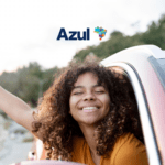 Mulher sorridente com a cabeça para fora da janela de um carro, aproveitando a viagem. Logo da Azul destacado na parte superior.