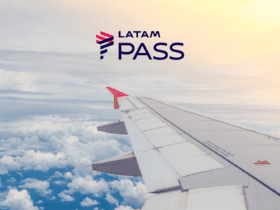 A imagem mostra a asa de um avião com uma ponta vermelha voando acima das nuvens. No canto superior direito, há o logotipo da LATAM Pass. O céu está parcialmente nublado, com o sol iluminando suavemente as nuvens. Pontos Latam Pass