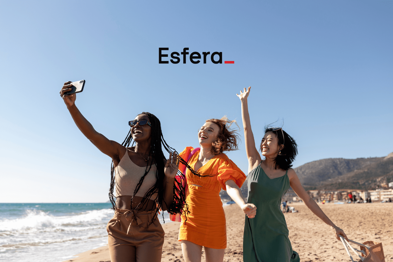 Pontos Esfera 50% OFF. Três mulheres sorrindo e tirando uma selfie em uma praia ensolarada, com o logotipo da Esfera no topo da imagem.
