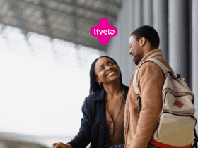 Imagem de um casal sorridente em um ambiente urbano, possivelmente uma estação de transporte. O homem está de mochila e casaco, e a mulher veste um casaco escuro, olhando para ele com um sorriso. Acima deles, no centro da imagem, está o logo da Livelo, indicando uma possível associação com programas de pontos ou viagens. Ganhe até 41 pontos Livelo.