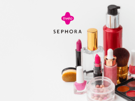 Ganhe até 9 pontos Livelo com a Sephora. A imagem mostra uma coleção de produtos de beleza incluindo batons, esmaltes, pincéis de maquiagem, um frasco de perfume e outros cosméticos, todos dispostos sobre uma superfície branca. No topo, centralizado, estão os logos da Livelo e da Sephora, com o logo da Livelo em rosa acima e o da Sephora em preto abaixo.