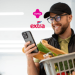 Homem sorridente segurando uma cesta de compras com vegetais, olhando para o celular. Acima dele, os logos da Livelo e do Extra, indicando uma parceria. Fundo claro e iluminado com luzes modernas. pontos esfera