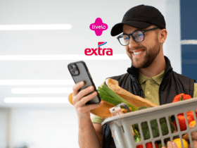Homem sorridente segurando uma cesta de compras com vegetais, olhando para o celular. Acima dele, os logos da Livelo e do Extra, indicando uma parceria. Fundo claro e iluminado com luzes modernas. pontos esfera