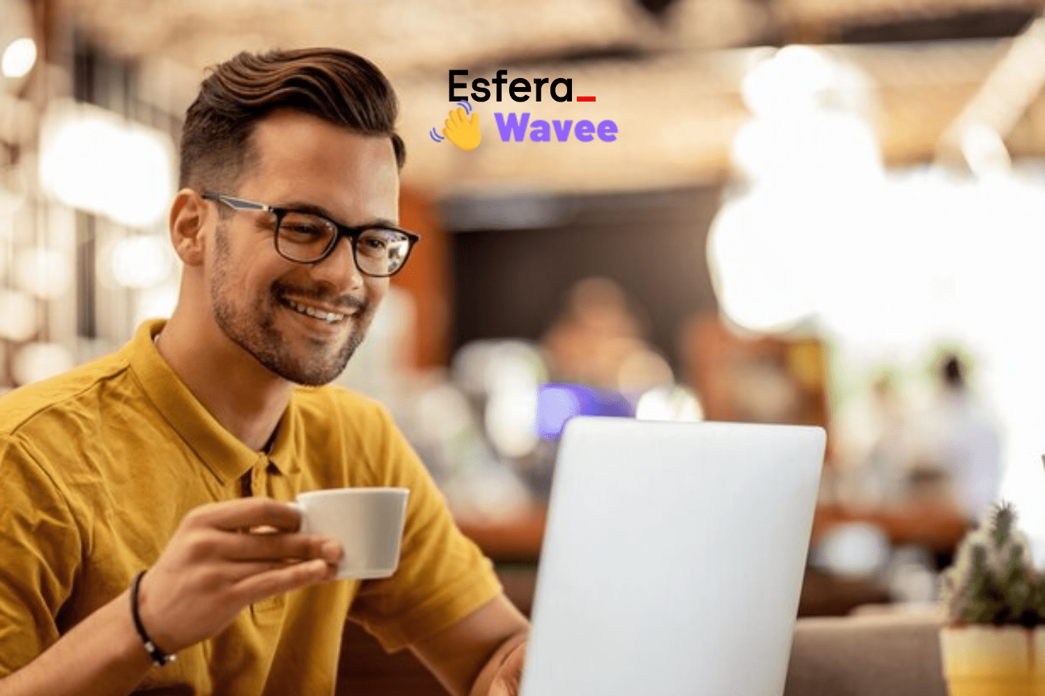 Homem jovem, com pele clara e óculos, usando uma camisa polo amarela, sorri enquanto segura uma xícara de café em uma mão e utiliza um laptop branco. Ele está sentado em uma cafeteria com o fundo desfocado, mostrando luzes e pessoas. No canto superior direito, estão os logotipos das marcas Esfera e Wavee