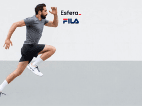 Na imagem, vemos um homem em movimento, capturado enquanto está correndo. Ele está usando uma camiseta cinza escura, shorts pretos e tênis brancos com detalhes coloridos, além de meias brancas. O fundo é dividido em duas partes, sendo a parte superior branca e a inferior cinza claro, criando um contraste que destaca o corredor. Acima da cabeça do homem, estão os logotipos da Esfera e da FILA, sugerindo uma colaboração ou promoção entre as marcas.