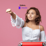 Imagem de uma jovem mulher em um fundo rosa, vestindo uma blusa branca de mangas compridas com detalhes de franjas. Ela está com o braço direito estendido para cima, como se estivesse imitando o voo do Superman. Em frente a ela, há uma mala vermelha. A expressão dela é confiante e alegre. No centro superior da imagem, estão os logos da Esfera e Decolar, sugerindo uma parceria entre as marcas.