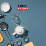 Imagem de utensílios de cozinha dispostos sobre uma superfície azul. Entre os itens visíveis estão um batedor manual, uma tábua de corte de madeira, um coador de metal, uma pequena jarra de vidro, uma batedeira manual, várias tigelas brancas, uma garrafa de vidro e uma chaleira branca. No canto superior direito, os logotipos da Esfera e da Polishop estão presentes, indicando uma parceria entre as duas marcas