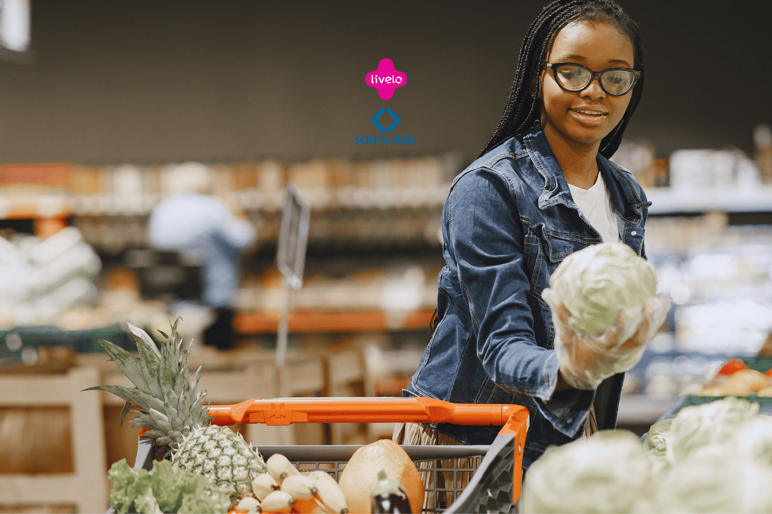 Imagem de uma jovem mulher fazendo compras em um supermercado. Ela está usando óculos, luvas e uma jaqueta jeans. A mulher segura uma cabeça de repolho enquanto olha para ele e sorri. Na frente dela, há um carrinho de compras parcialmente visível com diversos vegetais, incluindo um abacaxi. O fundo mostra prateleiras desfocadas com produtos. No centro superior da imagem, estão os logos da Livelo e do Sam's Club, sugerindo uma parceria entre as marcas