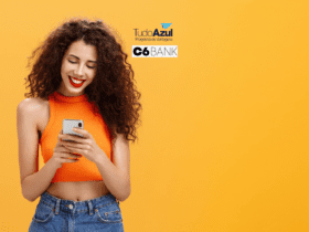 Imagem de uma mulher jovem com cabelo cacheado e longo, sorrindo enquanto olha para o seu smartphone. Ela está vestindo uma blusa cropped laranja sem mangas e calça jeans. O fundo é laranja sólido. No topo da imagem, há os logos 'TudoAzul Programa de Vantagens' e 'C6 Bank