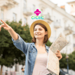 Na imagem, uma jovem mulher está em um ambiente urbano, usando um chapéu de palha e uma camisa jeans sobre uma camiseta branca. Ela segura um mapa na mão esquerda e aponta para algo à sua frente com a mão direita, enquanto sorri. Ao fundo, há prédios e árvores que compõem o cenário. Na parte superior central da imagem, estão os logotipos das empresas Livelo e Ciclic.