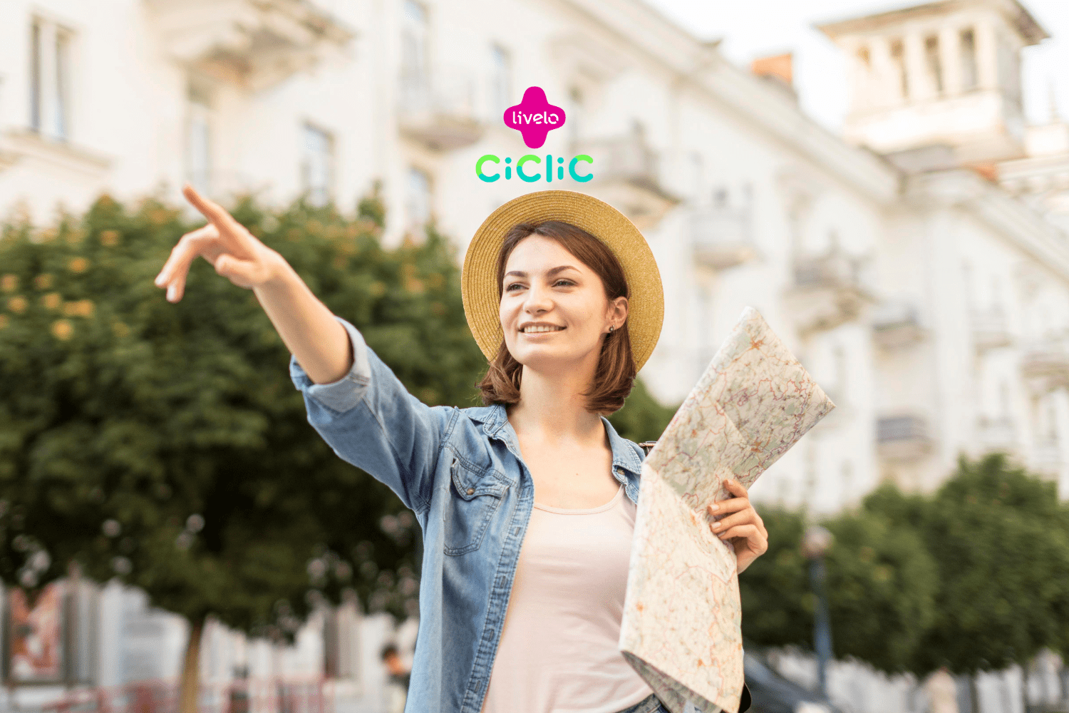 Na imagem, uma jovem mulher está em um ambiente urbano, usando um chapéu de palha e uma camisa jeans sobre uma camiseta branca. Ela segura um mapa na mão esquerda e aponta para algo à sua frente com a mão direita, enquanto sorri. Ao fundo, há prédios e árvores que compõem o cenário. Na parte superior central da imagem, estão os logotipos das empresas Livelo e Ciclic.