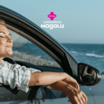 Na imagem, uma mulher está relaxando dentro de um carro, com a janela aberta, de frente para o mar. Ela está com os olhos fechados e um sorriso sereno no rosto, sentindo a brisa marítima. A mulher usa uma camisa xadrez de mangas longas arregaçadas. No fundo, vemos o mar azul e um céu claro. Na parte superior central da imagem, estão os logotipos das empresas Livelo e Consórcio Magalu.