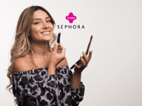 Na foto, uma mulher sorridente aplica batom enquanto segura um celular na outra mão. Ela veste uma blusa ombro a ombro com estampa de leopardo em tons de preto e cinza. Os logotipos da Livelo e Sephora aparecem no topo da imagem."