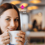 Uma mulher jovem com cabelos castanhos claros e lisos, que vão até os ombros, está sentada em um ambiente de café. Ela sorri levemente enquanto segura uma xícara branca de café próxima ao rosto, parecendo saborear a bebida. A mulher está usando brincos pequenos e uma camisa azul clara. O fundo da imagem está desfocado, mostrando luzes suaves e o interior do café com um ambiente acolhedor. No topo da imagem, estão os logotipos "livelo" em rosa e "Coffee ++