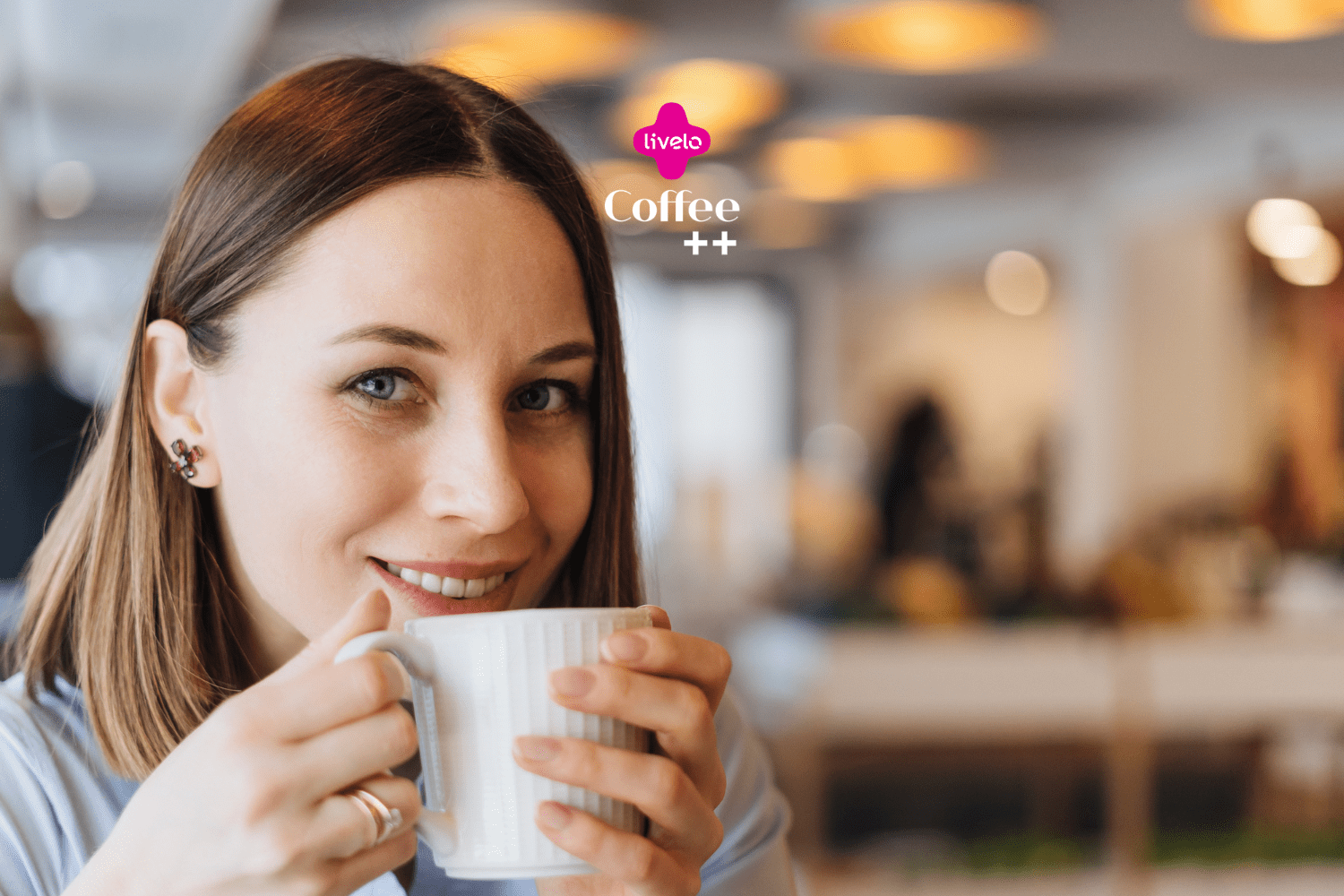 Uma mulher jovem com cabelos castanhos claros e lisos, que vão até os ombros, está sentada em um ambiente de café. Ela sorri levemente enquanto segura uma xícara branca de café próxima ao rosto, parecendo saborear a bebida. A mulher está usando brincos pequenos e uma camisa azul clara. O fundo da imagem está desfocado, mostrando luzes suaves e o interior do café com um ambiente acolhedor. No topo da imagem, estão os logotipos "livelo" em rosa e "Coffee ++