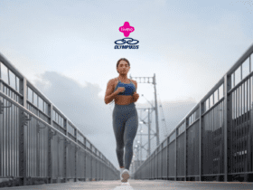 A imagem mostra uma mulher correndo em uma ponte com grades metálicas altas de ambos os lados. Ela veste um top azul e uma calça legging cinza, complementados por tênis brancos. O fundo da imagem exibe um céu parcialmente nublado. Acima da mulher, estão os logotipos da Livelo e da Olympikus, centralizados na parte superior da imagem.