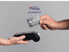 Duas mãos aparecem na imagem contra um fundo cinza claro. Uma mão, à esquerda, segura uma máquina de cartão de crédito. A outra mão, à direita, está segurando um cartão de crédito preto, pronto para ser inserido ou aproximado da máquina. Acima das mãos, estão os logos da LATAM Pass e Credicard.