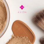 Imagem de maquiagem com um pote de pó facial bege à esquerda, uma base líquida marrom clara espalhada no centro, e dois pincéis de maquiagem à direita. Os logotipos da Livelo e da Avon estão no topo, em destaque sobre um fundo branco.