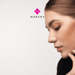 "Uma mulher com cabelo castanho claro, preso em um coque elegante, está de perfil contra um fundo branco. Ela usa um brinco dourado com um design geométrico em forma de losango, adornado com padrões em preto e dourado. Na mão, ela exibe um anel dourado que complementa o brinco. A expressão no rosto dela é serena e concentrada. Acima, estão os logotipos das marcas 'Livelo' em rosa e 'Morana' em preto".