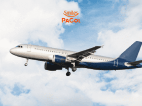 Um avião comercial de fuselagem azul e prata voa em meio ao céu azul com algumas nuvens brancas. Acima do avião, está o logo laranja da Smiles PaGol, indicando uma parceria ou promoção relacionada a viagens aéreas. A imagem transmite a sensação de liberdade e aventura associada a voar.