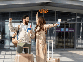 Casal sorridente em frente a um aeroporto, segurando passagens aéreas e levantando os braços em comemoração. Eles têm malas de viagem ao lado. Acima deles está o logo da Smiles, indicando uma viagem feliz e recompensadora.