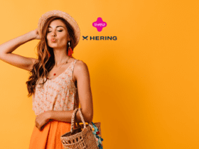 Mulher jovem, vestida de forma leve e casual, usando chapéu de palha e bolsa de vime, fazendo um biquinho e posando contra um fundo amarelo vibrante. Acima dela, estão os logos da Livelo e da Hering, sugerindo uma parceria de moda e estilo.