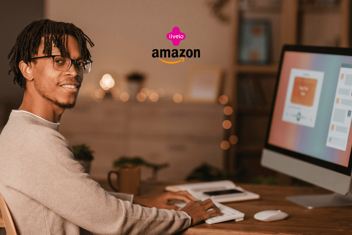 Homem negro com cabelo trançado e óculos, sorrindo para a câmera enquanto trabalha em um computador de mesa em um ambiente aconchegante. No canto superior, os logos da Livelo e da Amazon aparecem juntos.