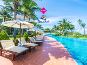 Piscina em um resort cercada por espreguiçadeiras com guarda-sóis brancos, palmeiras e um céu azul claro. Acima da cena, estão os logos da Livelo e do Beach Park, sugerindo um ambiente de lazer e relaxamento em um destino tropical.