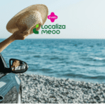 Pessoa dentro de um carro à beira-mar, estendendo o braço para fora da janela e segurando um chapéu de palha, com o oceano ao fundo. Acima, estão os logos da Livelo e da Localiza Meoo, sugerindo uma viagem relaxante.