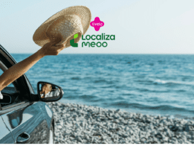 Pessoa dentro de um carro à beira-mar, estendendo o braço para fora da janela e segurando um chapéu de palha, com o oceano ao fundo. Acima, estão os logos da Livelo e da Localiza Meoo, sugerindo uma viagem relaxante.