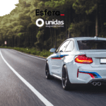 Carro esportivo branco dirigindo em alta velocidade por uma estrada cercada de árvores. Acima do carro, estão os logos da Esfera e da Unidas Aluguel de Carros, sugerindo uma viagem emocionante e confortável.