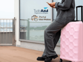 Pessoa encostada em uma mala rosa, segurando um celular, com uma varanda ao fundo. No canto superior esquerdo da imagem, estão as logos do programa de vantagens "TudoAzul" e "Portal das Malas".