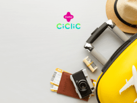 Uma mala amarela com um chapéu de palha e uma miniatura de avião estão ao lado de um passaporte, uma câmera vintage, passagens aéreas e uma pequena quantia de dinheiro em dólar enrolada. As logos da "Livelo" e "Ciclic" estão posicionadas acima da imagem.