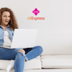 Uma mulher jovem, sentada em um sofá branco, está usando um laptop no colo e segurando um cartão de crédito na mão, com uma expressão de surpresa e alegria. Acima dela, no centro da imagem, estão as logos da Livelo e do AliExpress