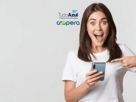 Uma mulher com expressão de surpresa e empolgação segura um smartphone na mão direita enquanto aponta para ele com a mão esquerda. Ela veste uma camiseta branca e tem cabelos castanhos. Acima dela, estão as logos do TudoAzul Programa de Vantagens e da Coopera.