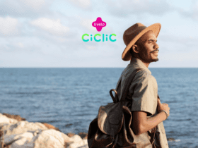 Homem negro usando um chapéu e mochila, olhando para o horizonte enquanto está à beira-mar. Acima dele, estão os logos da Livelo e da Ciclic, sugerindo uma parceria entre as duas marcas.